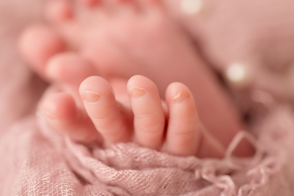 Close-up detail of tiny newborn baby toes wrapped in pink lace fabric.