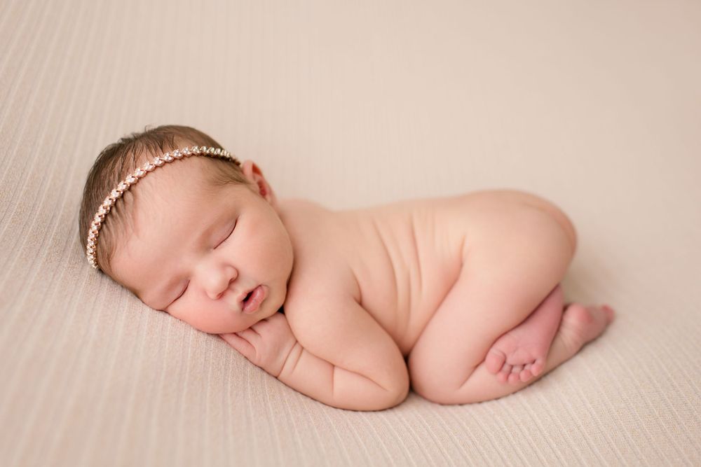 Sleeping newborn with delicate gold headband posed on cream textured backdrop.