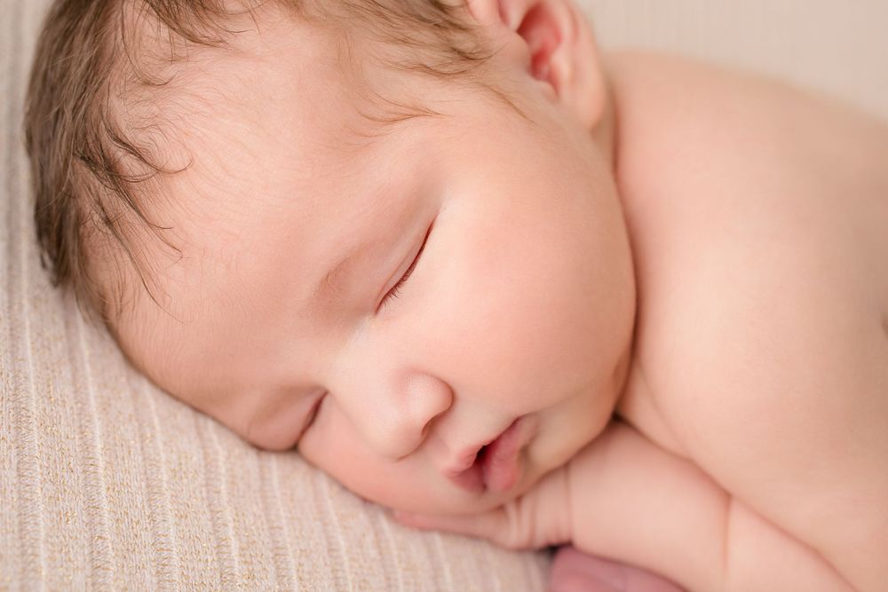 Peaceful sleeping newborn baby resting on soft beige fabric in natural light.