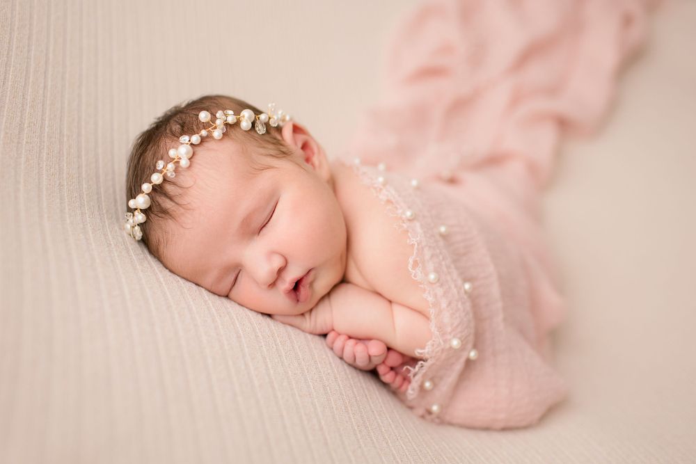 Sleeping newborn wrapped in pink lace fabric wearing delicate pearl headpiece.