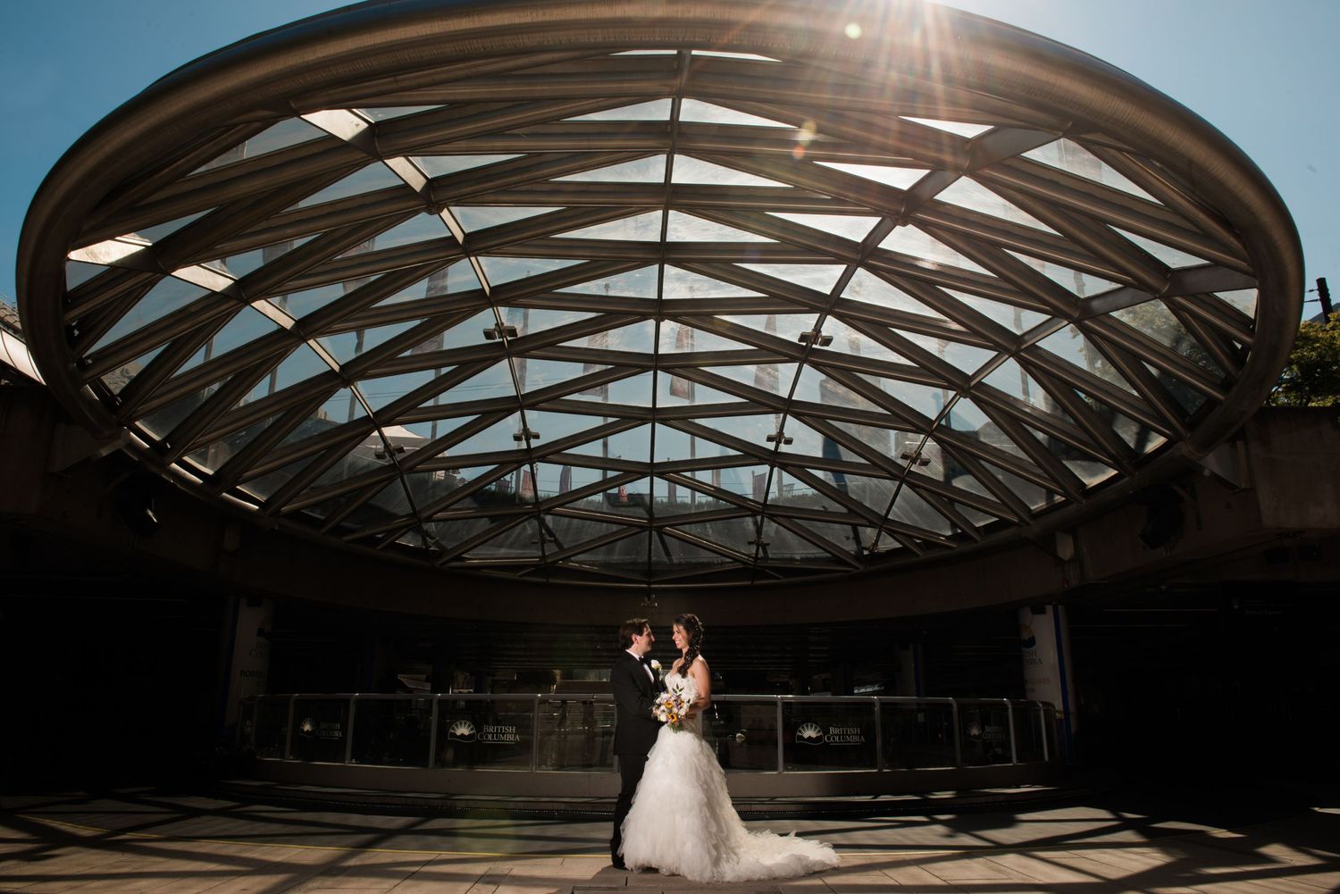 A dramatic wedding photo under an architectural glass dome ceiling with sunburst lighting.