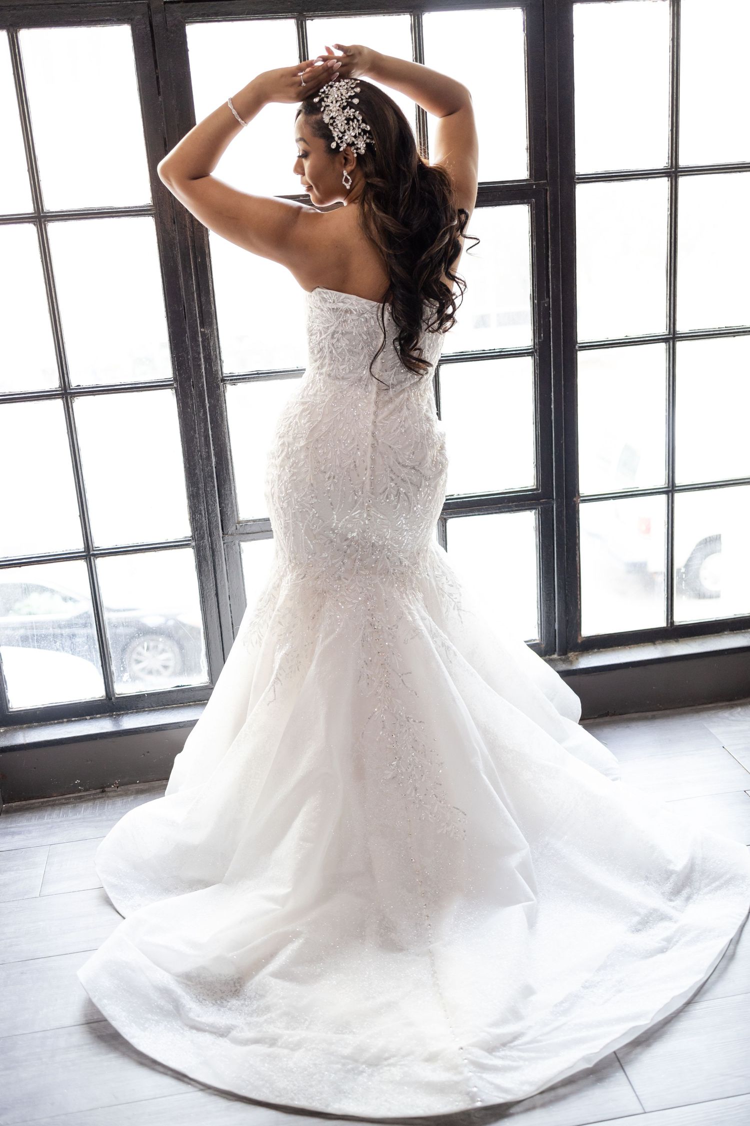 Bride in fitted lace wedding gown poses against window backlight.