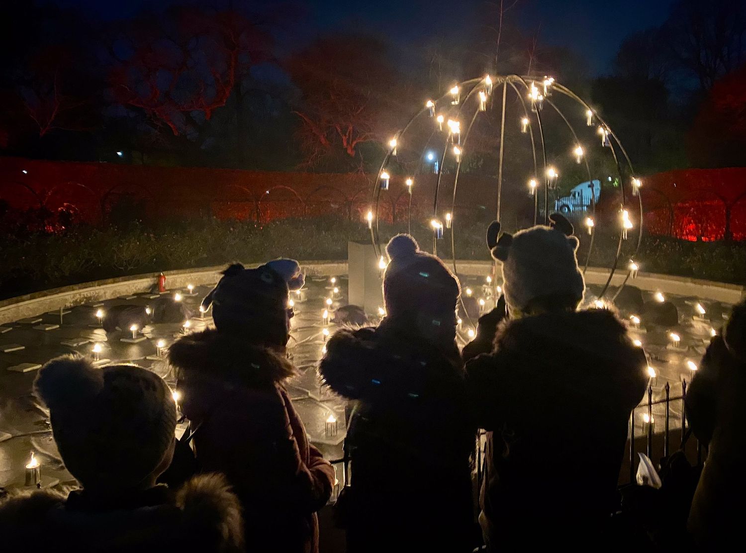 Silhouettes of people watching a glowing light arch installation at night.