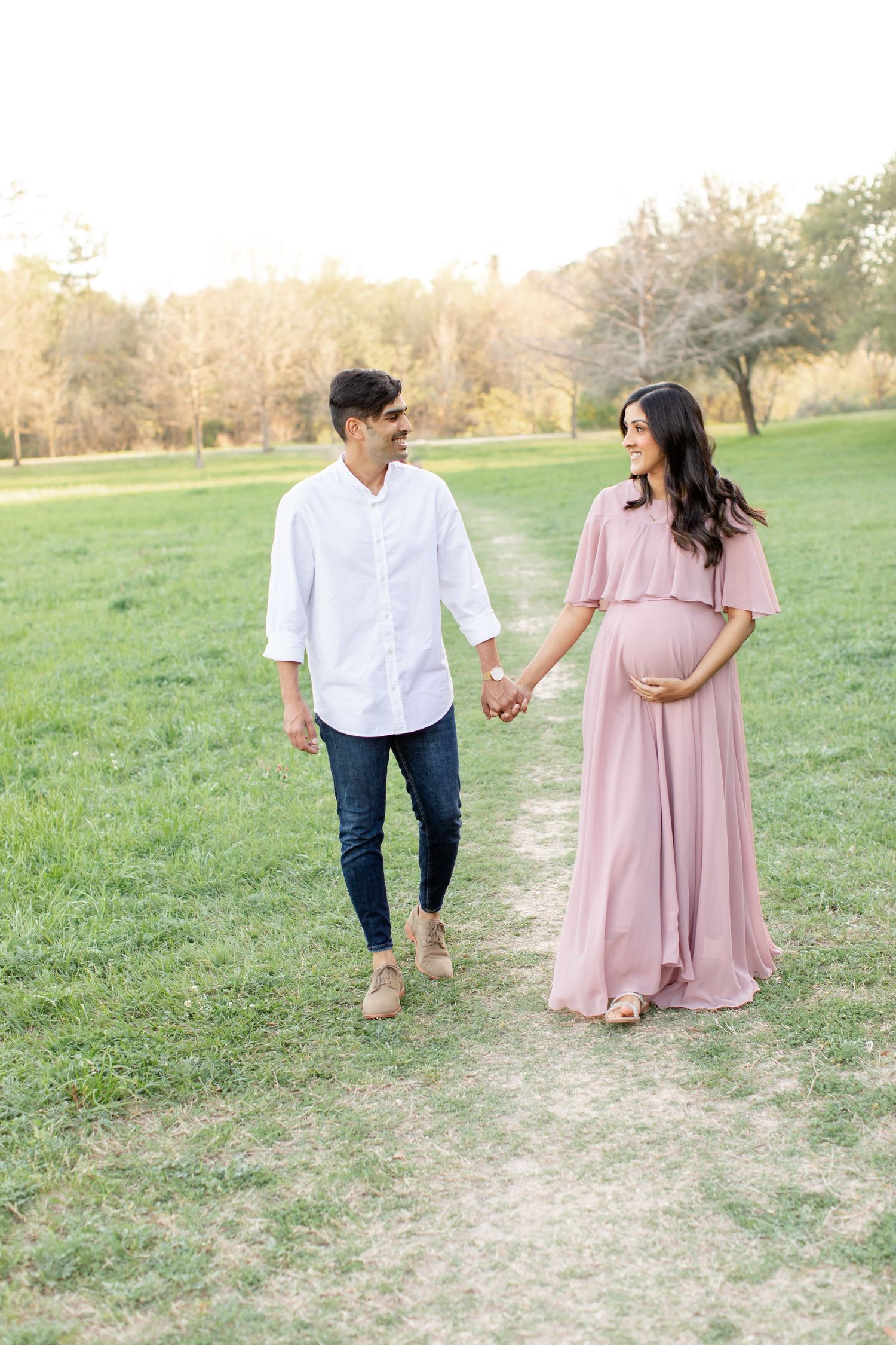 A couple strolls hand in hand on a grassy trail during golden hour.