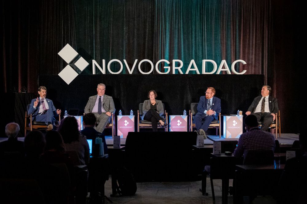 A panel discussion takes place on stage under the Novogradac logo with speakers seated in a row.