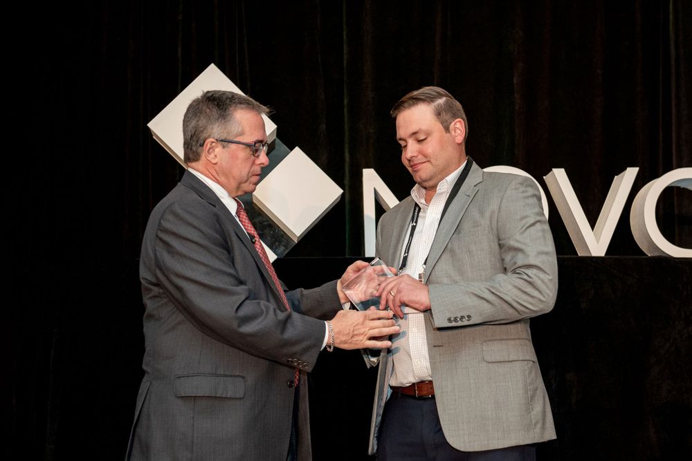 Two business professionals examine an award or trophy together on stage at a corporate event.