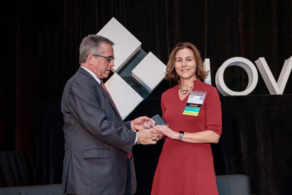 Two professionals exchange an award or certificate on stage at a Novogradac corporate event.