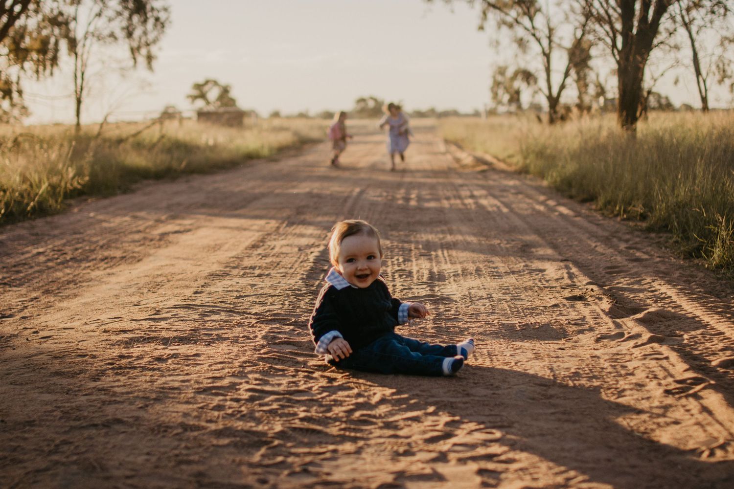 little boy playing on a dirt road with his sister running around in the background at sunset