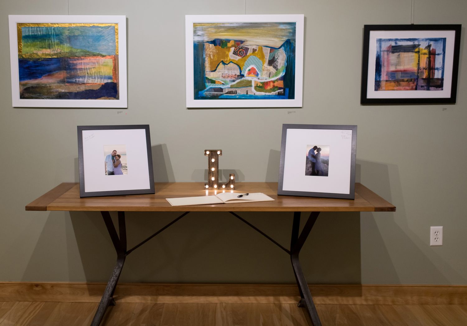 Gallery wall display featuring framed artwork and photographs on a gray wall with wooden shelf.