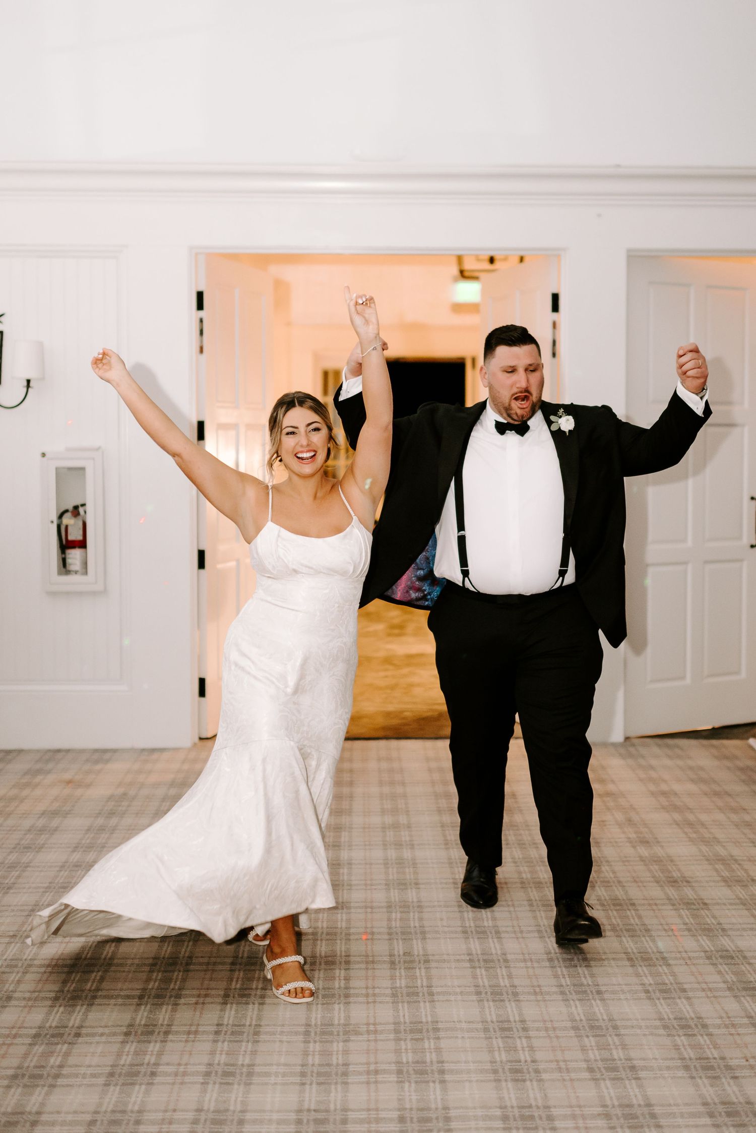 Wedding couple performs fun dance moves across a light-colored ballroom floor.