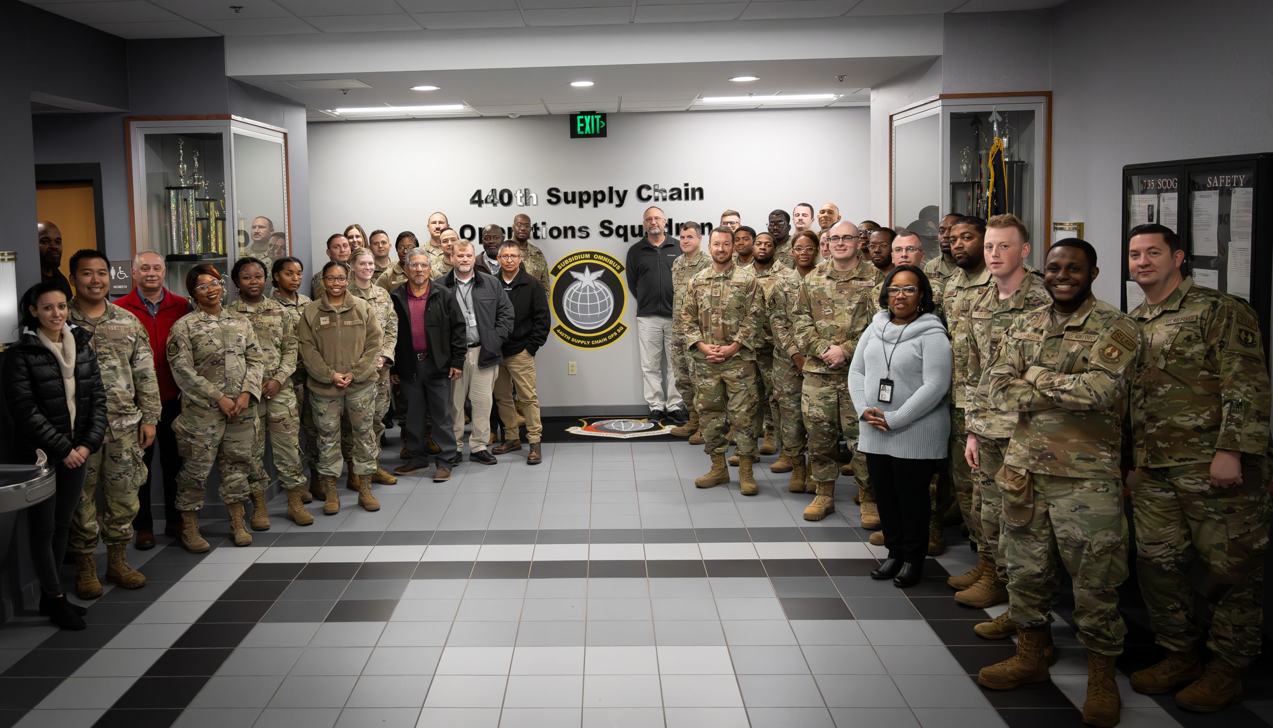 Military personnel assembled in formation inside a building hallway with a unit crest displayed.
