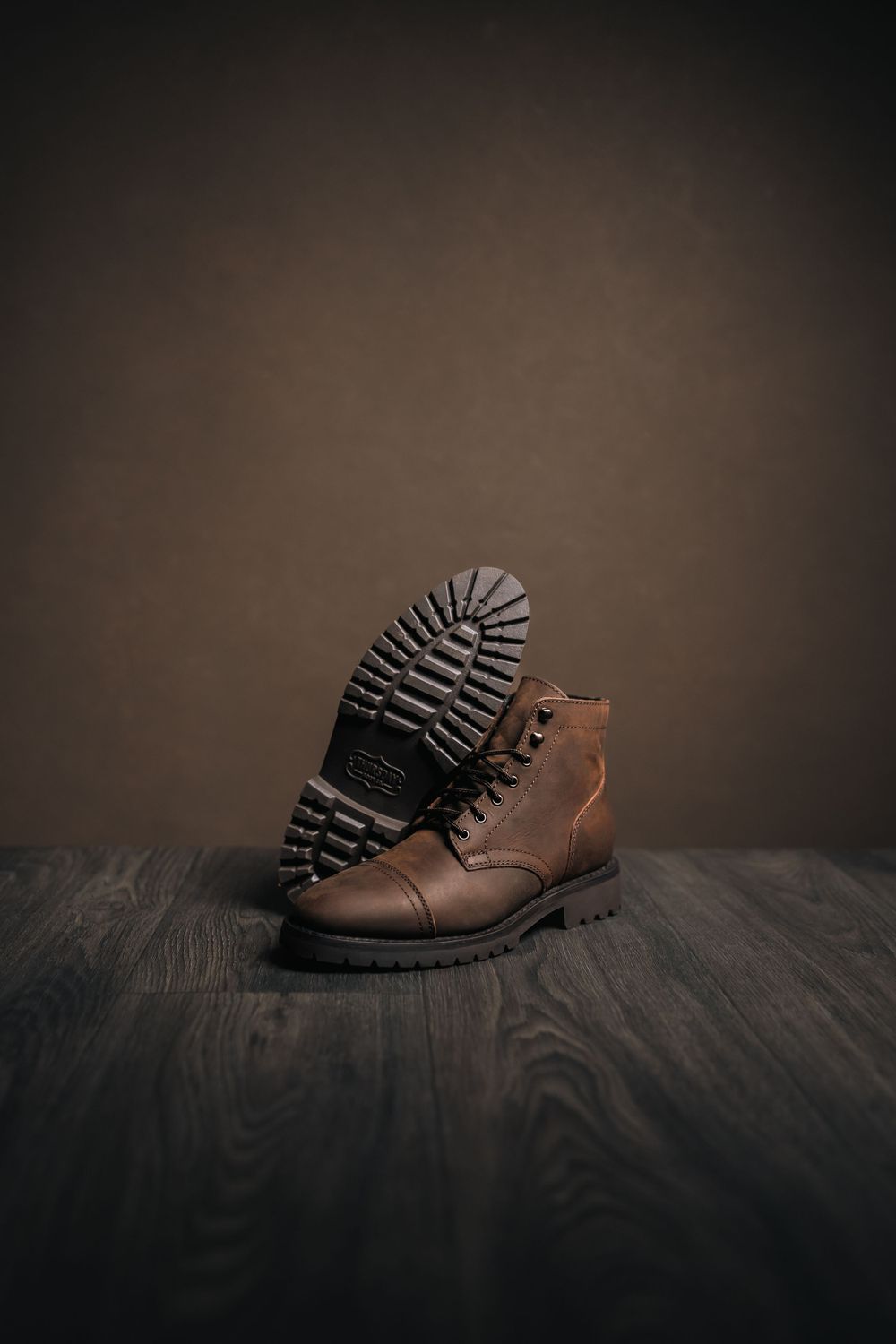 A brown leather boot with rugged sole displayed on dark wooden flooring.
