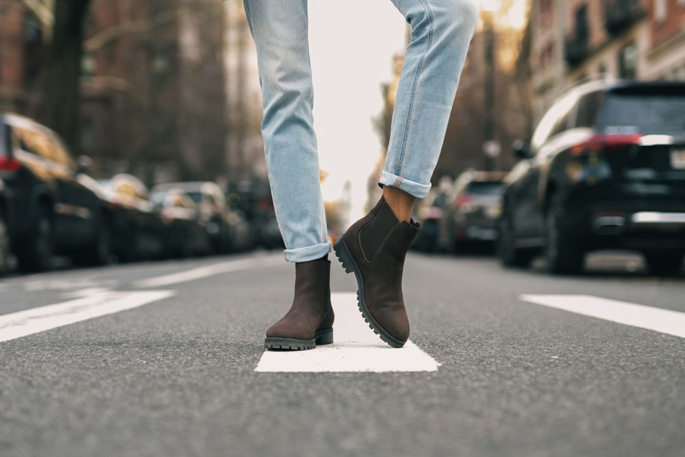 Person walking on city street wearing light denim jeans and white sneakers.