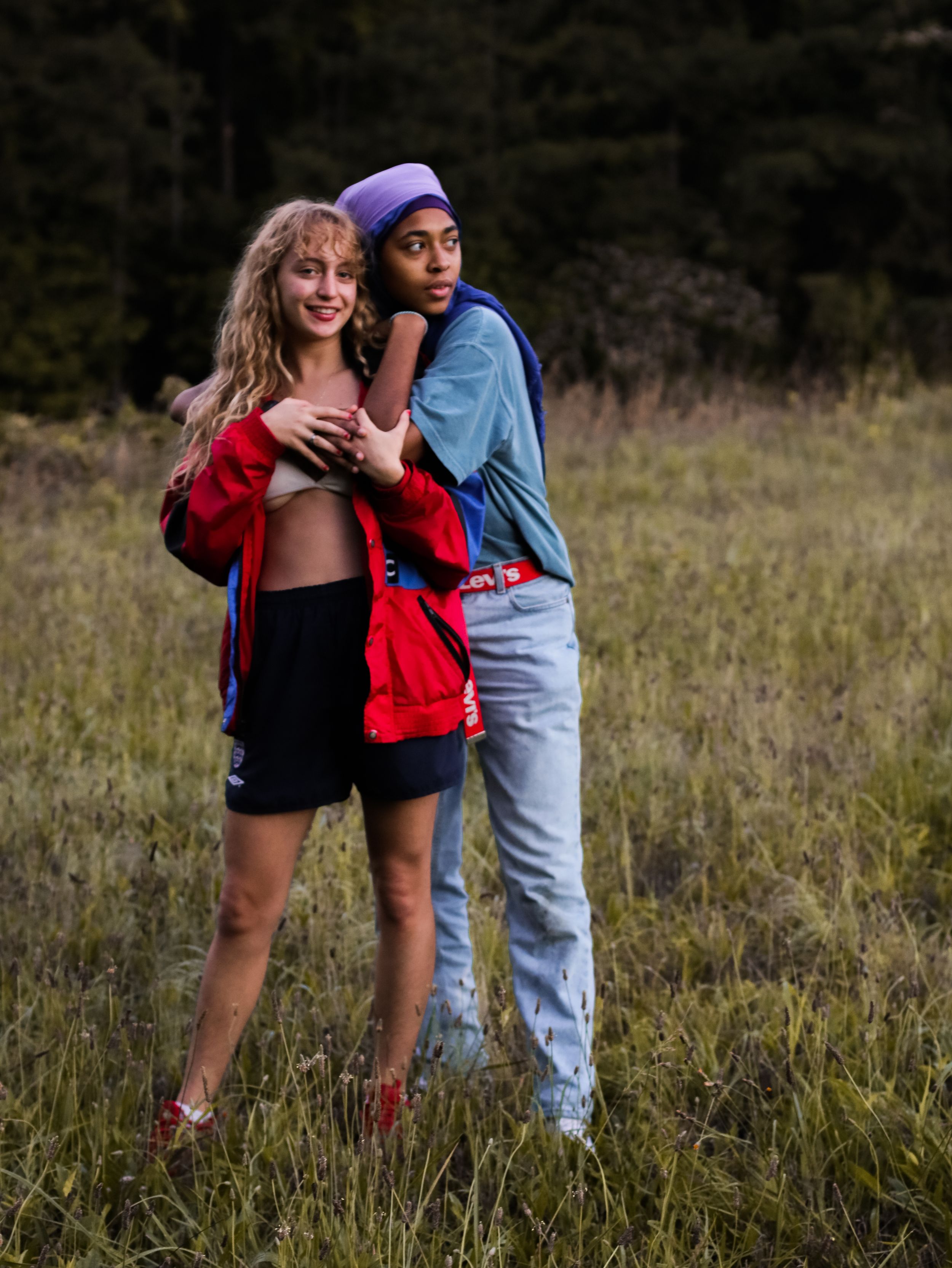 Couple poses playfully in a grassy field at sunset wearing casual attire.