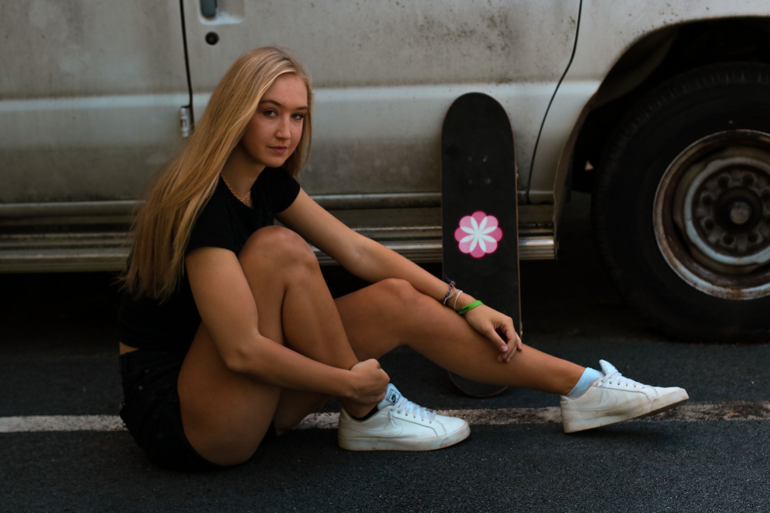 Woman in athletic wear sits casually next to a car tire in an urban setting.
