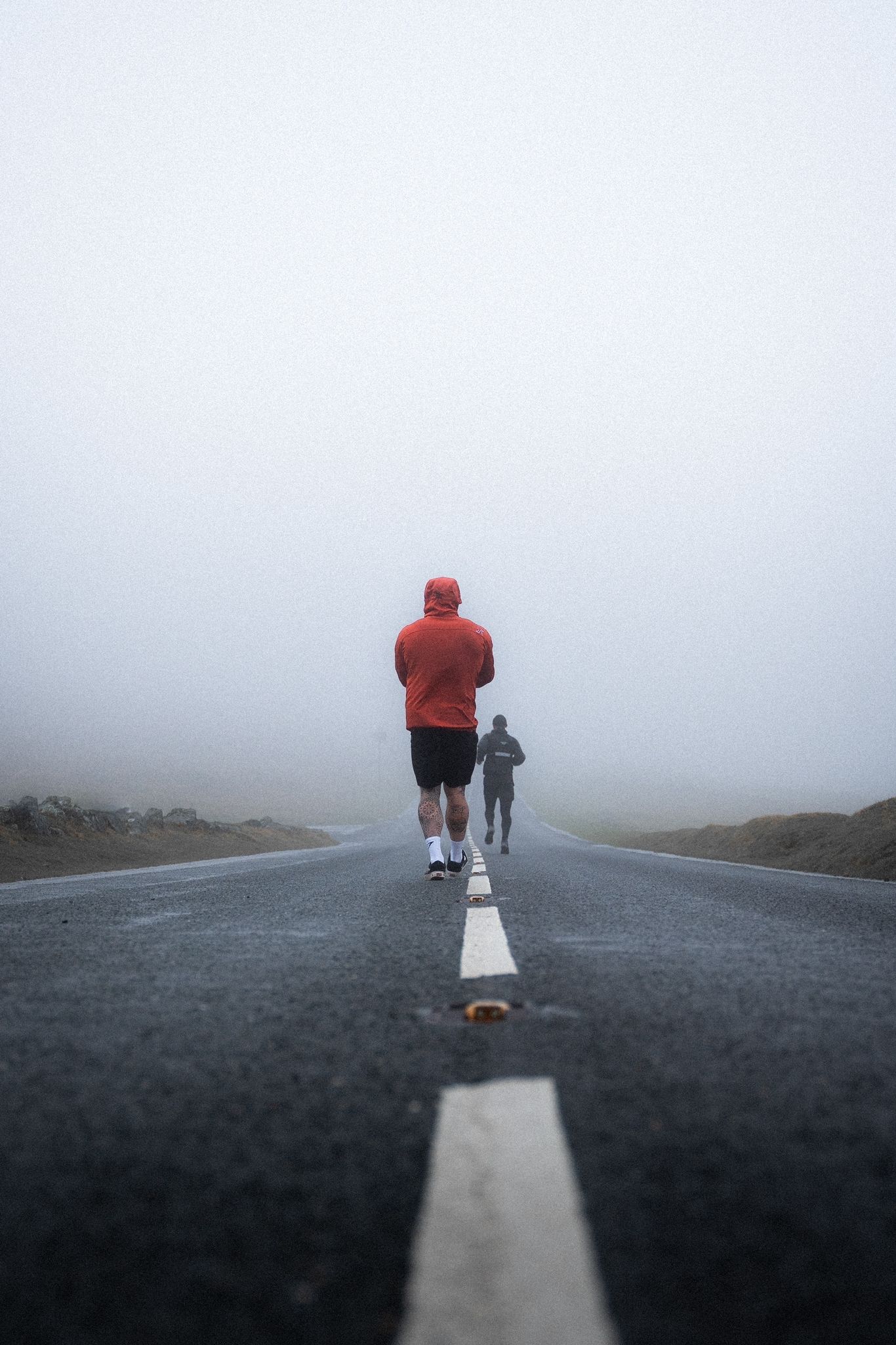 Runner on foggy road with white dividing line stretching into misty horizon.
