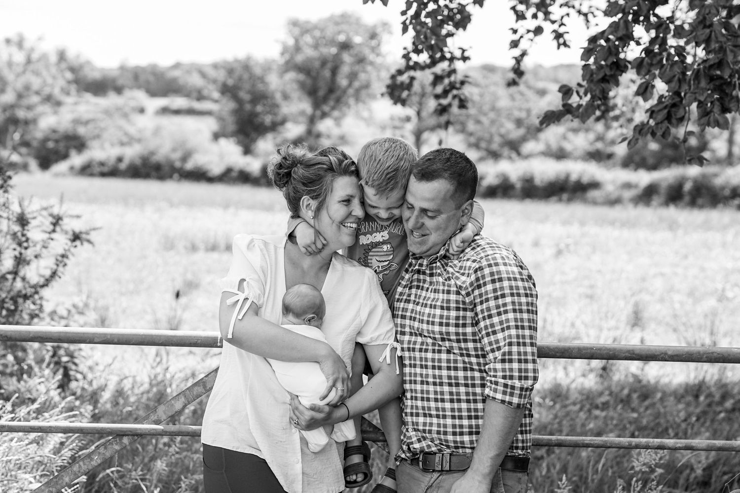 Happy family sharing a candid moment together by rustic fence in countryside setting.