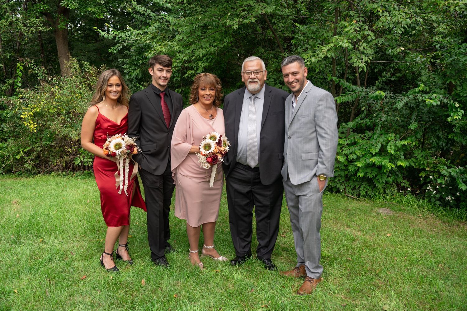 Wedding party poses together on green lawn surrounded by lush foliage.