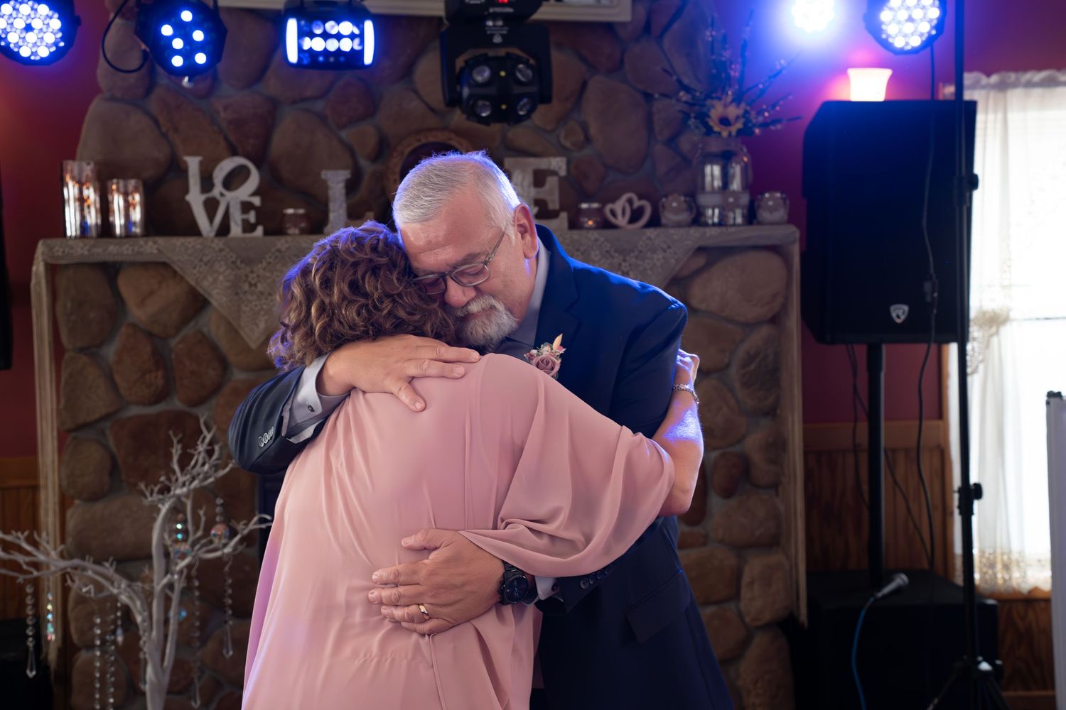 Wedding reception dance with dramatic blue lighting and stone wall backdrop.