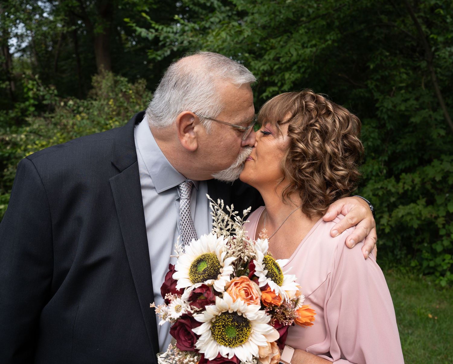 Couple shares romantic moment during outdoor wedding ceremony with floral bouquet.