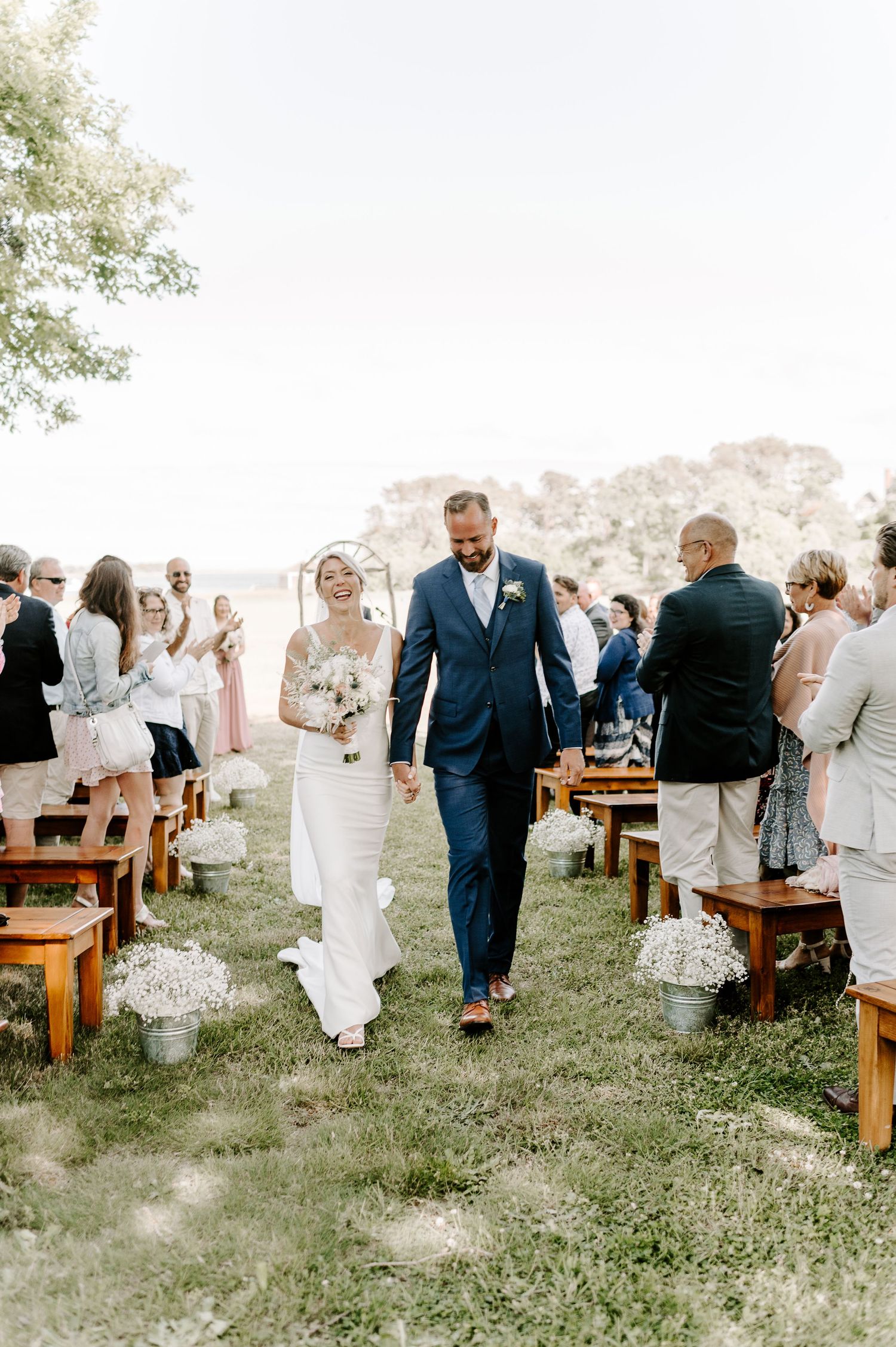 Wedding guests gather on wooden benches for an outdoor hillside ceremony.