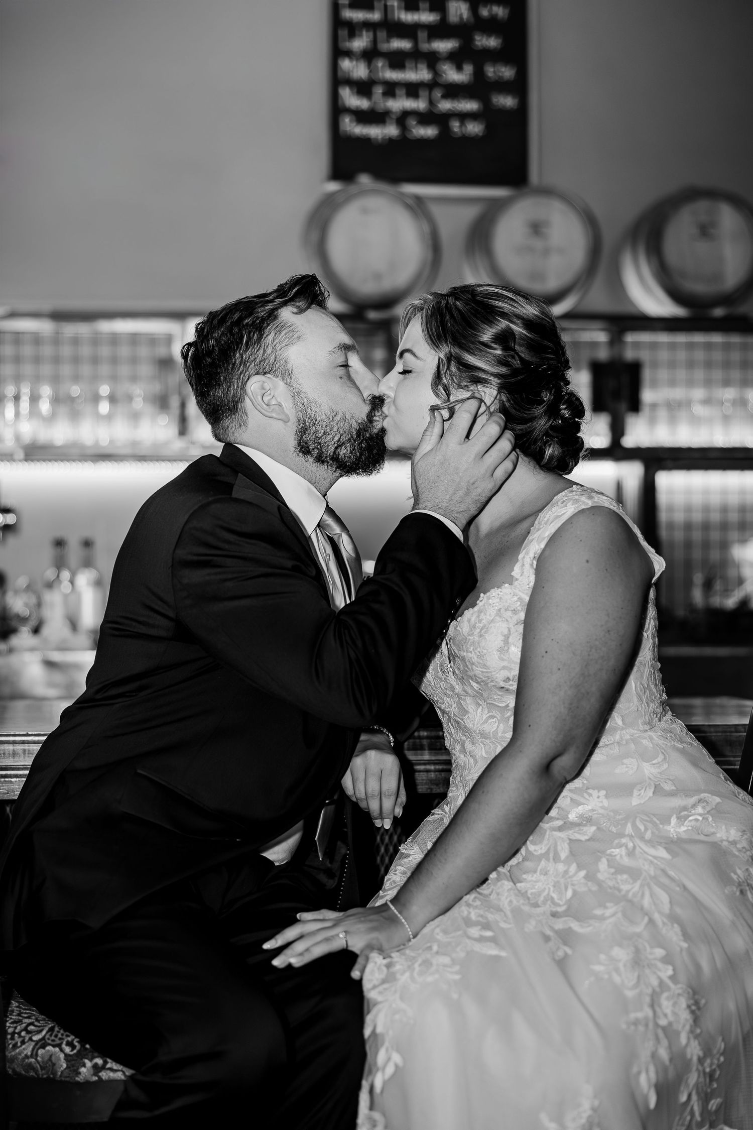 An intimate black and white moment of a couple kissing at a rustic bar setting.