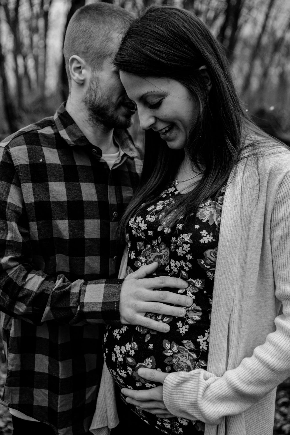 Tender maternity moment captured in black and white with plaid shirt and floral dress.