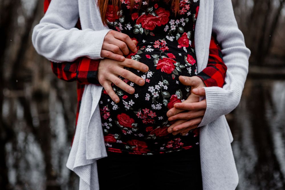 Close-up of hands cradling pregnant belly in floral dress with white cardigan.