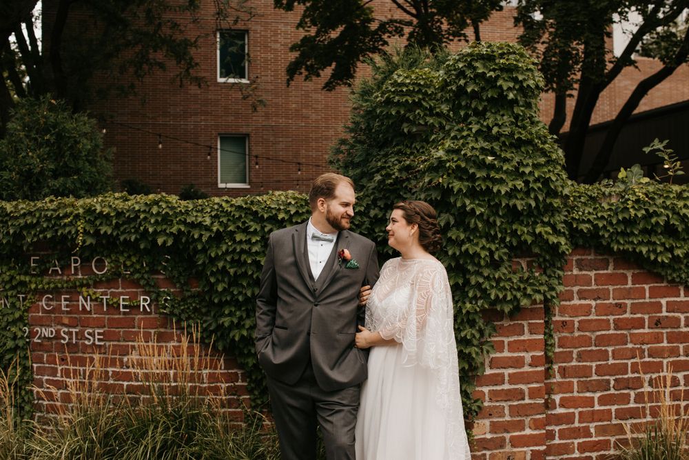 Bride and groom share a loving glance in front of ivy-covered brick building sign outdoors.