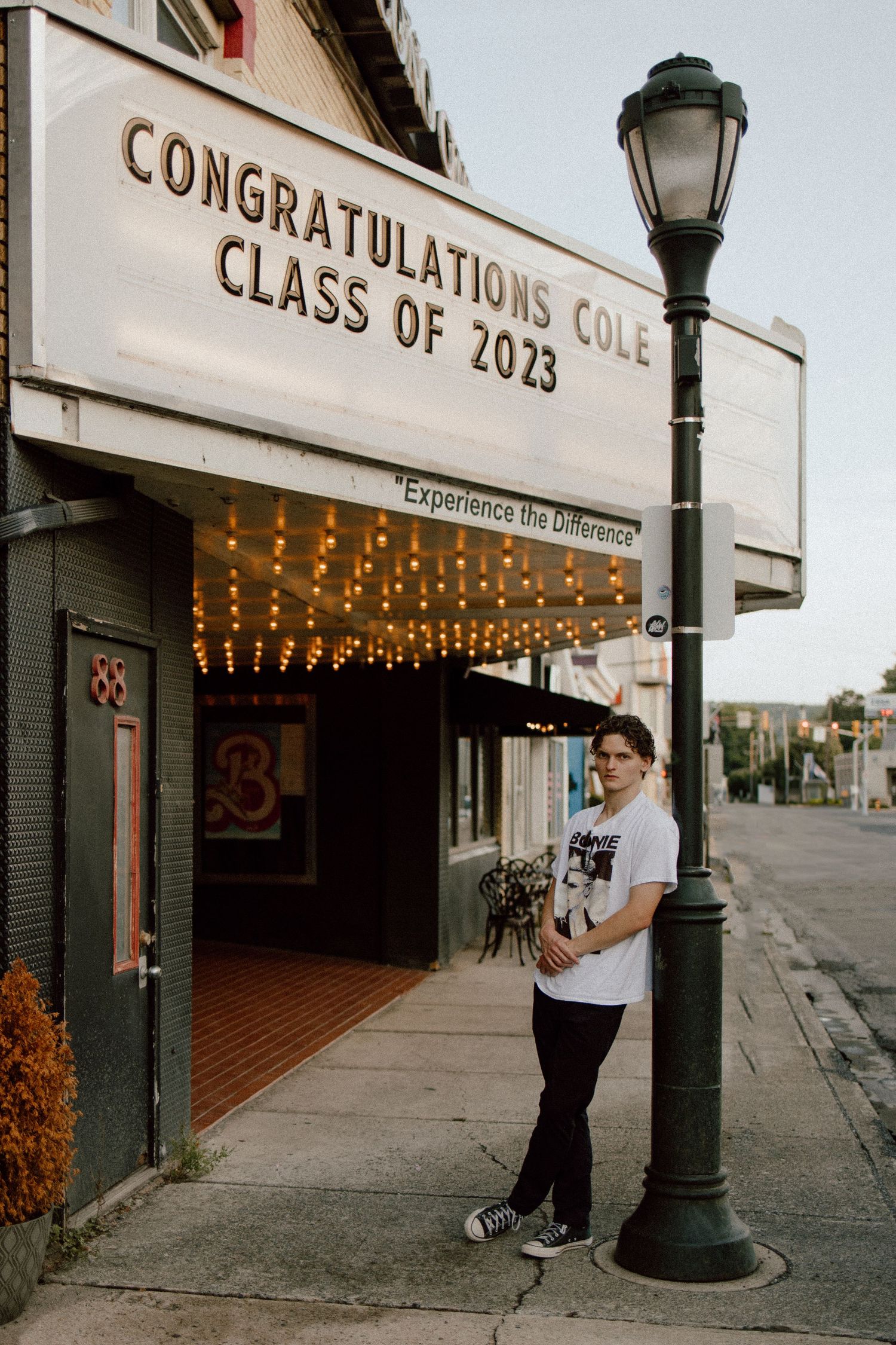 Graduate stands by vintage lamp post under Class of 2023 congratulations sign.