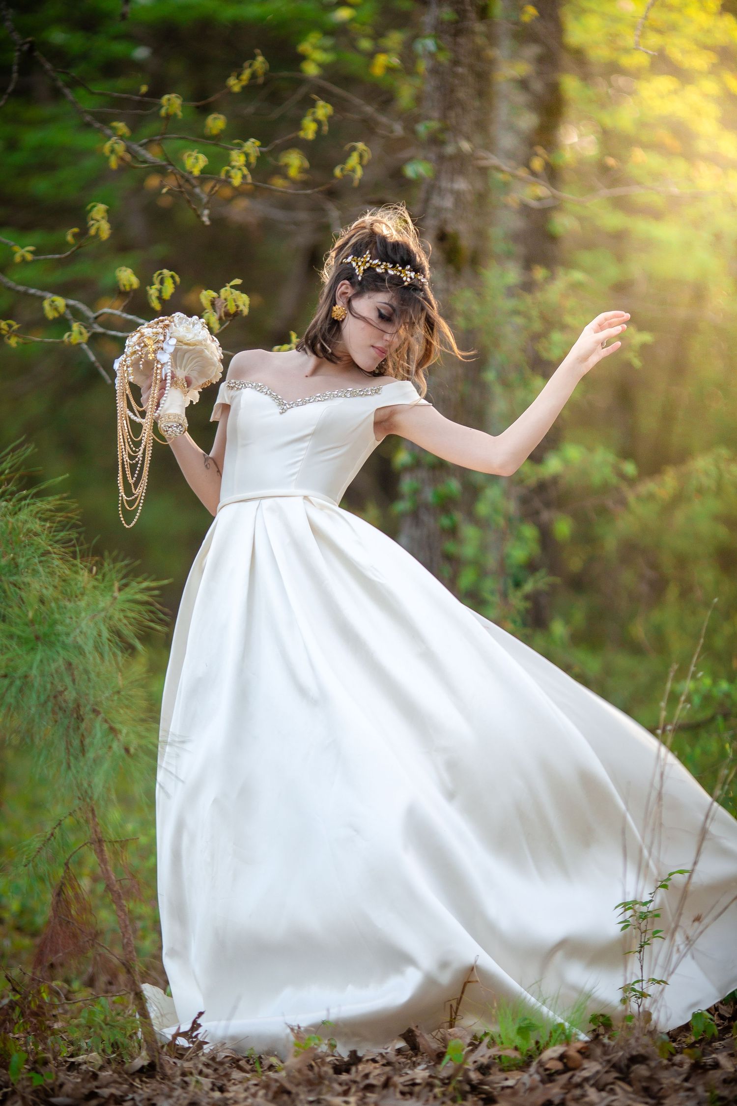 Bride in a flowing white gown twirling in a sunlit forest holding a bouquet.
