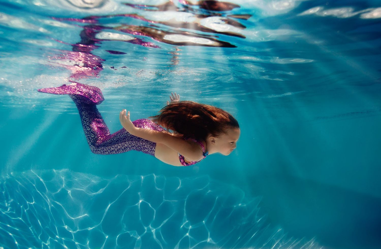 Underwater swimming photography with rippling blue water and streams of sunlight.