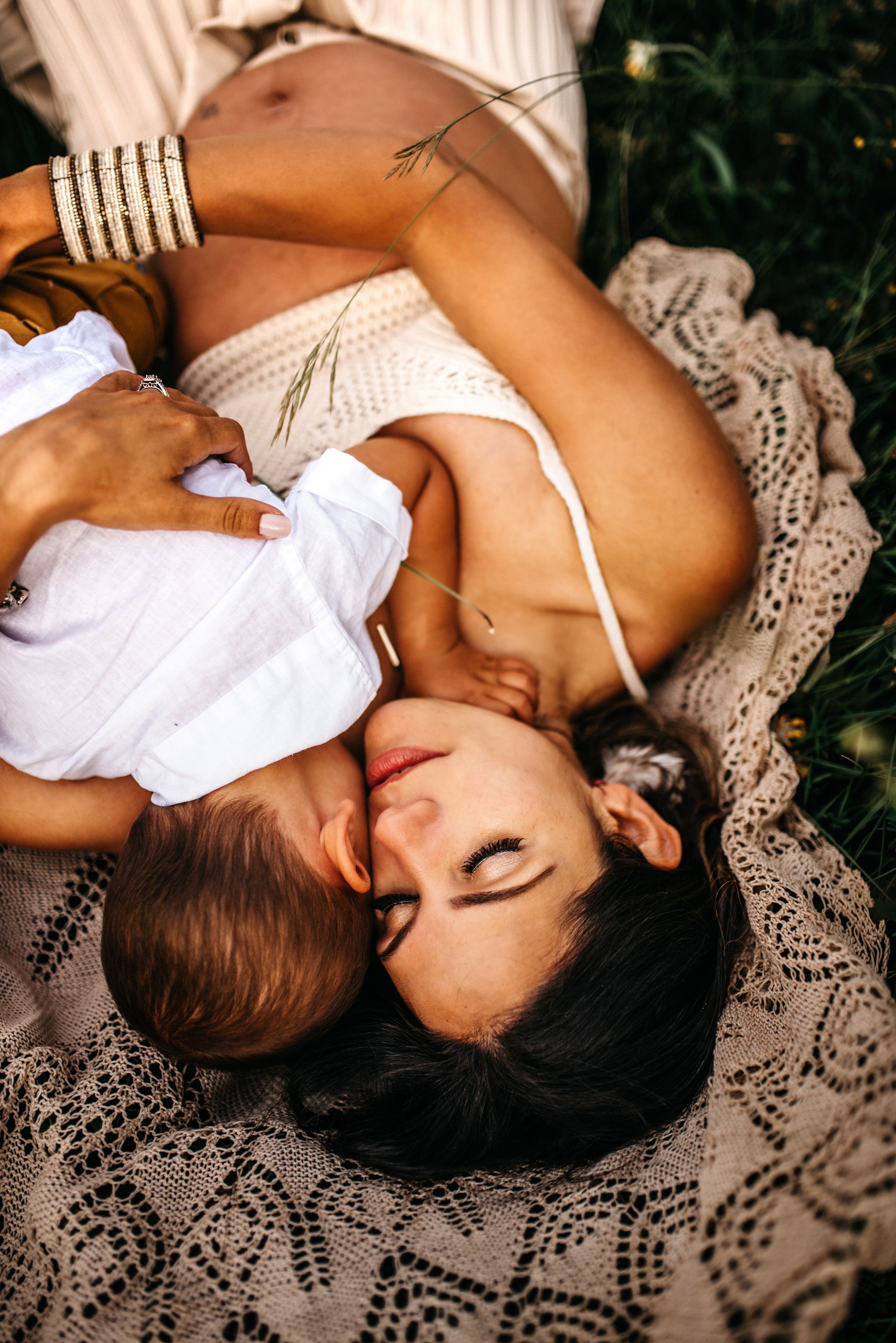 Mommy and me portrait with mother and son laying on a lace blanket in a field in Asiago, Italy.