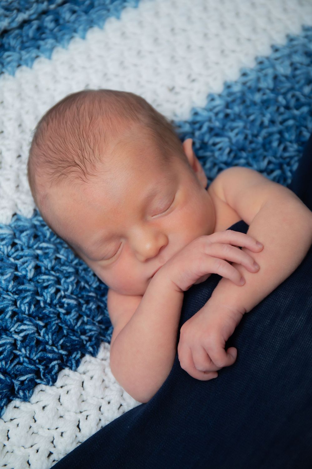 Newborn sleeping peacefully on striped blue and white knitted blanket.