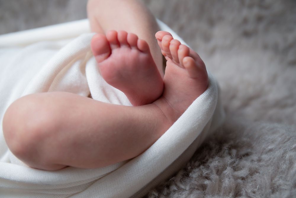 Close-up of tiny newborn baby feet wrapped in white fabric on gray textured background.