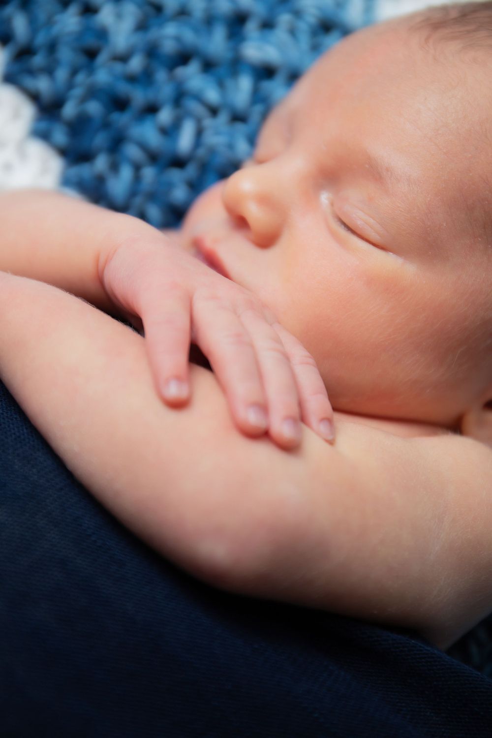 Peaceful sleeping newborn with hand near face on blue knitted blanket.