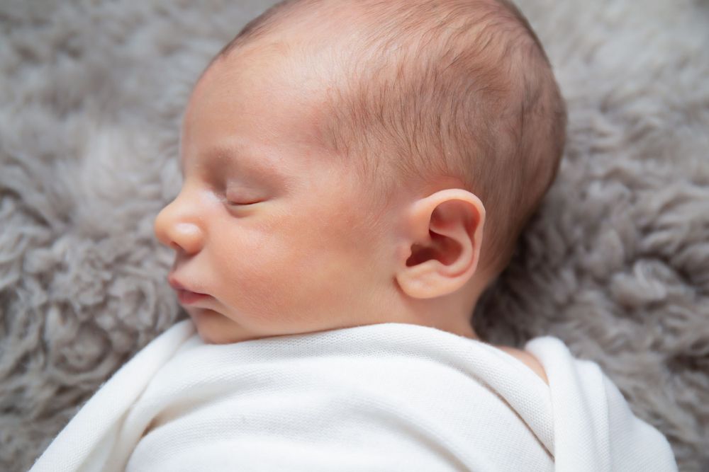 Profile view of sleeping newborn on soft gray furry blanket.