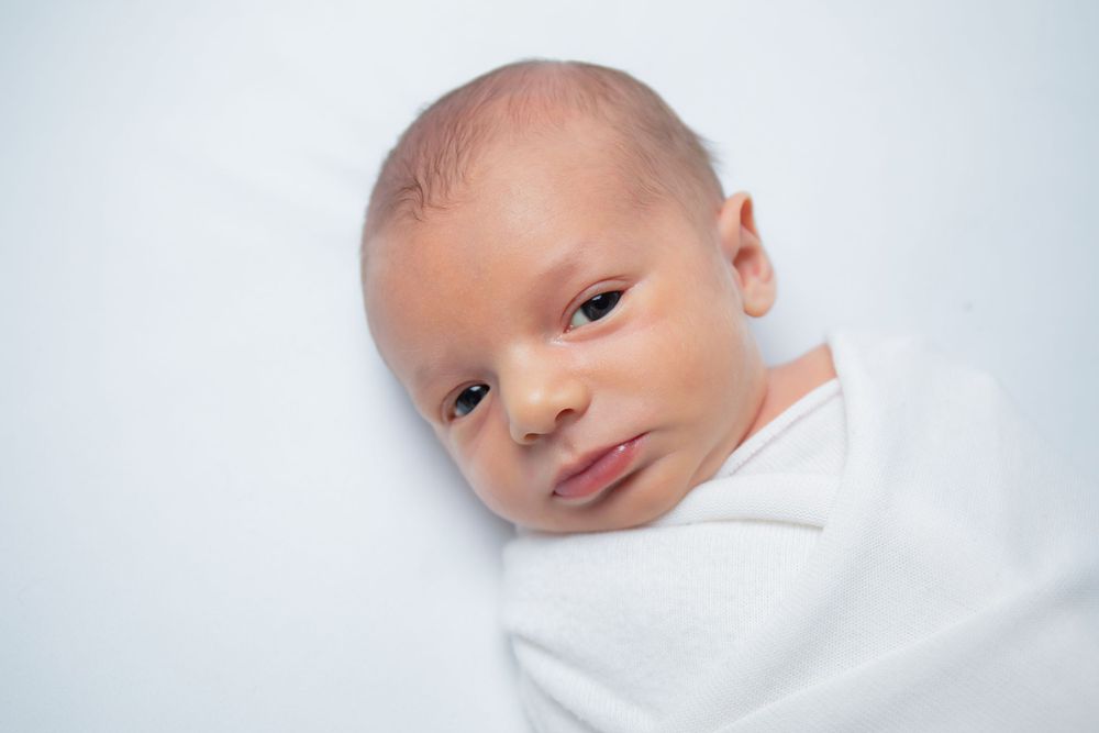 Close up portrait of newborn baby swaddled in white against light background.