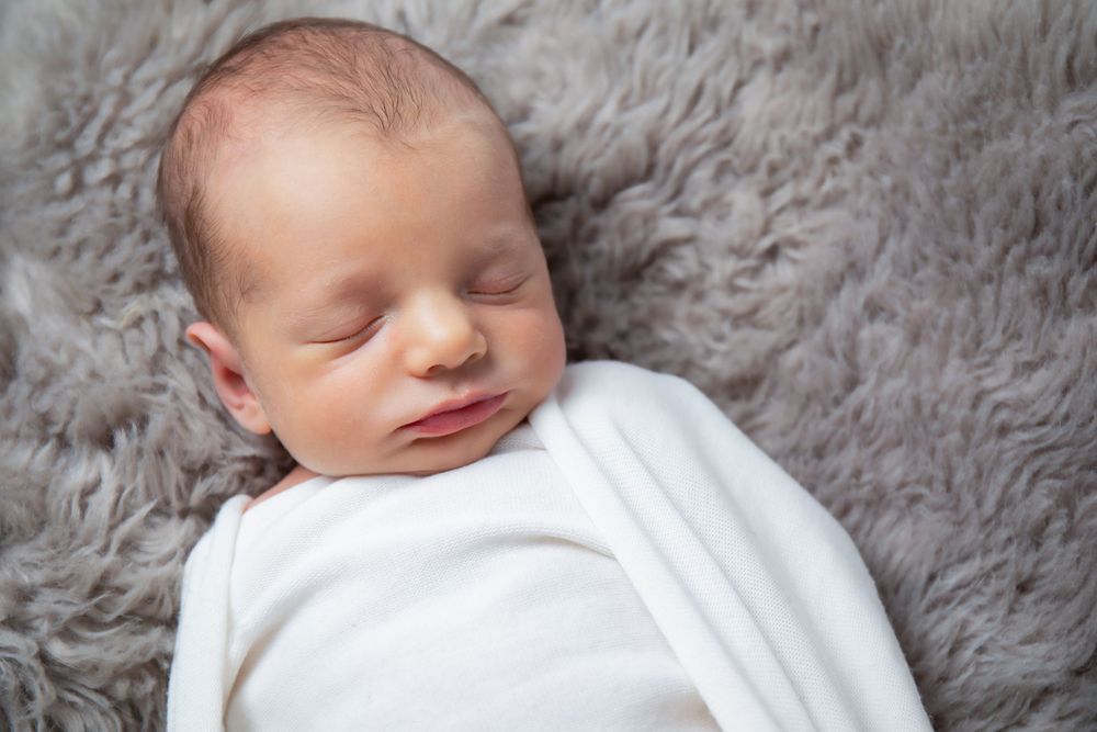 Sweet sleeping baby wrapped in white on plush gray background.
