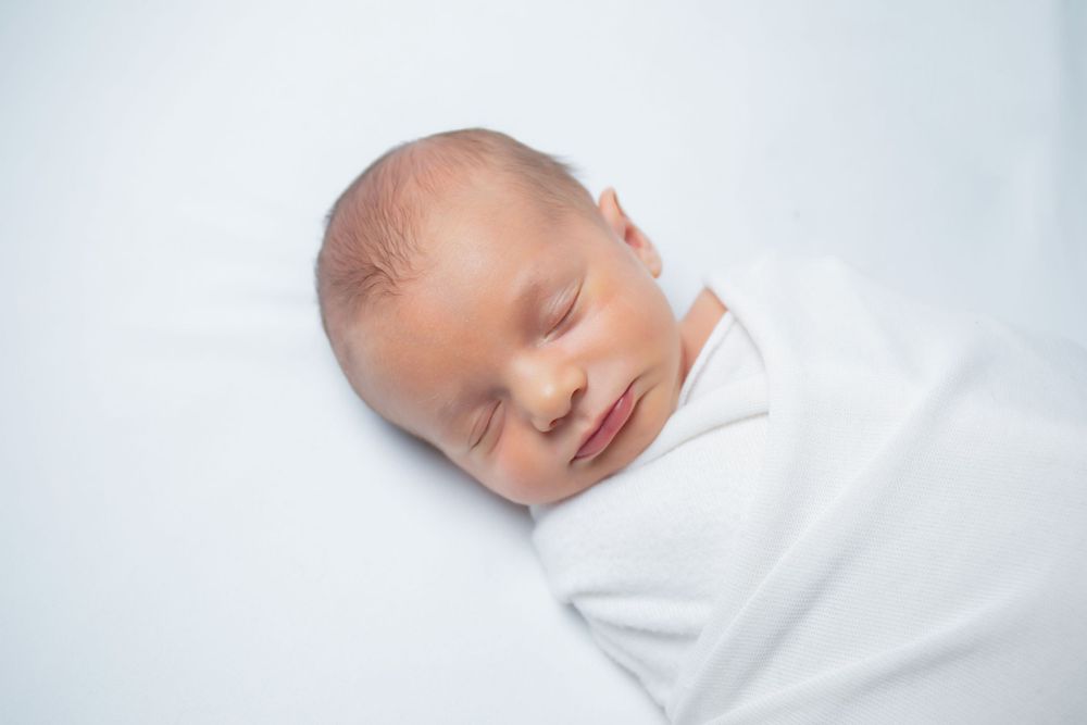 Sweetly sleeping newborn baby swaddled in white blanket on light background.