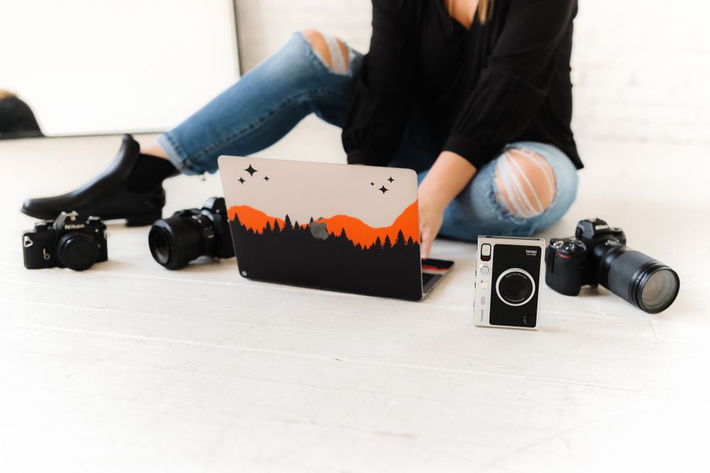 Photography workspace setup with camera gear and laptop on white floor.