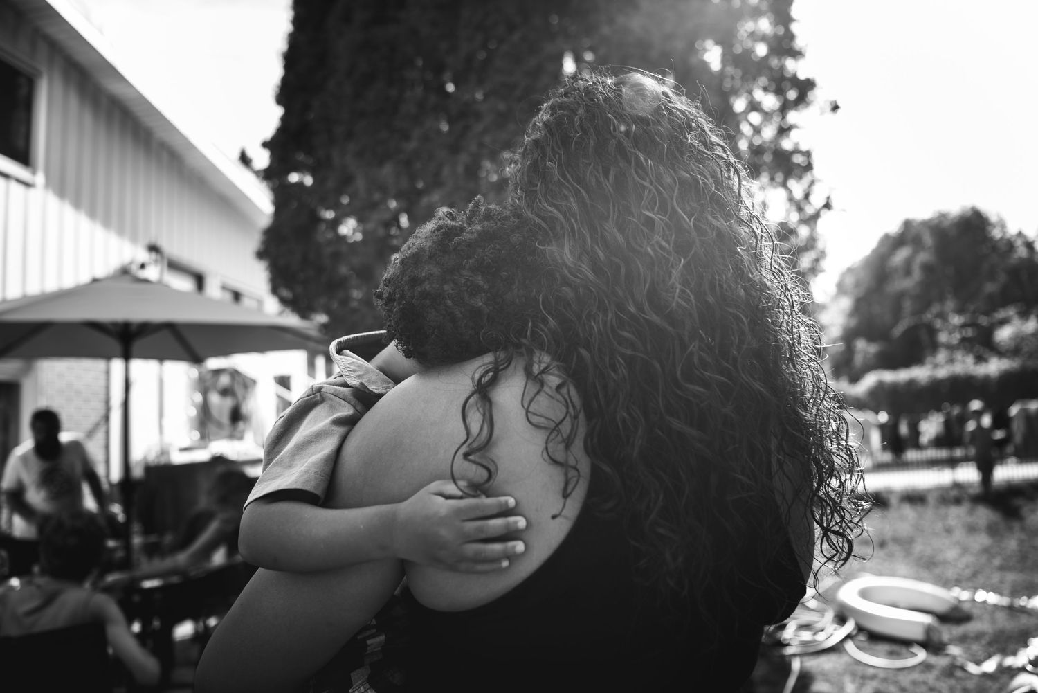 BW image from behind of a woman holding her young son as he places his little hand on her arm.