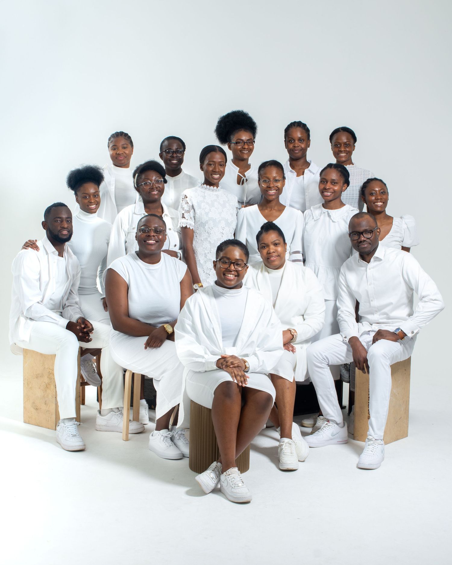 Large group of Black individuals posing together in matching all-white outfits against a white background.