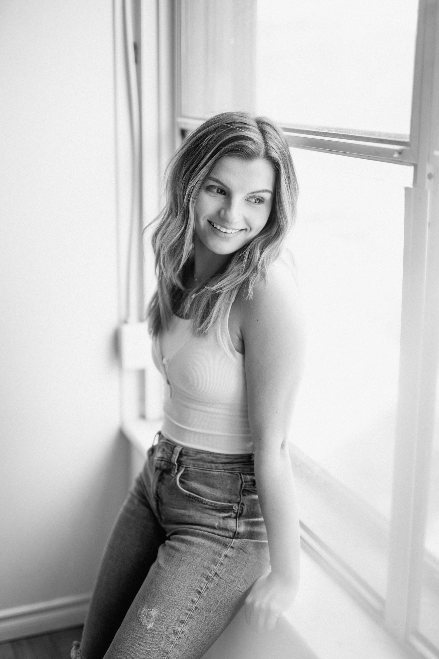 Natural window light portrait in casual attire with soft black and white tones.