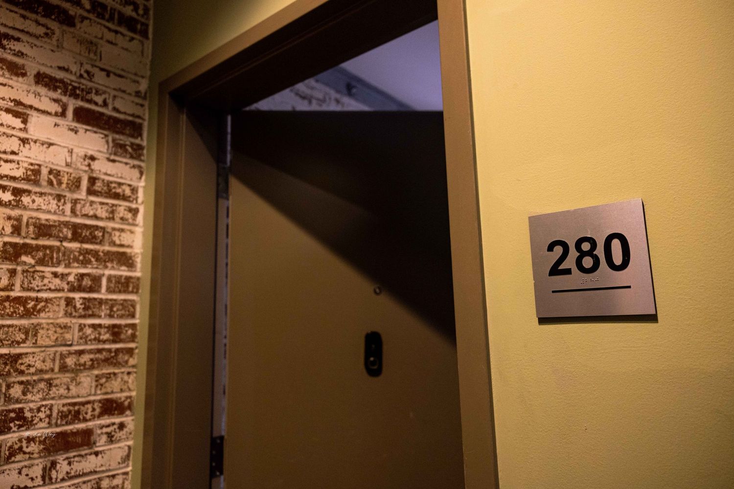 Room number 280 sign mounted on yellow wall next to exposed brick.