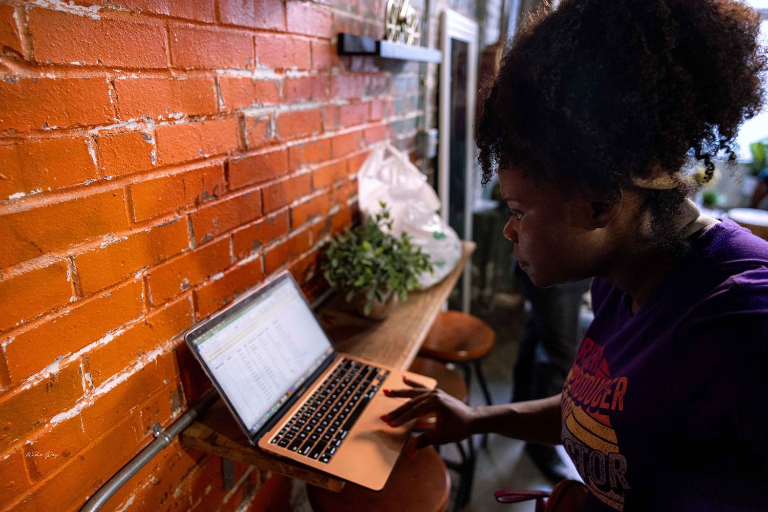 Person working on laptop next to orange brick wall with potted plants.