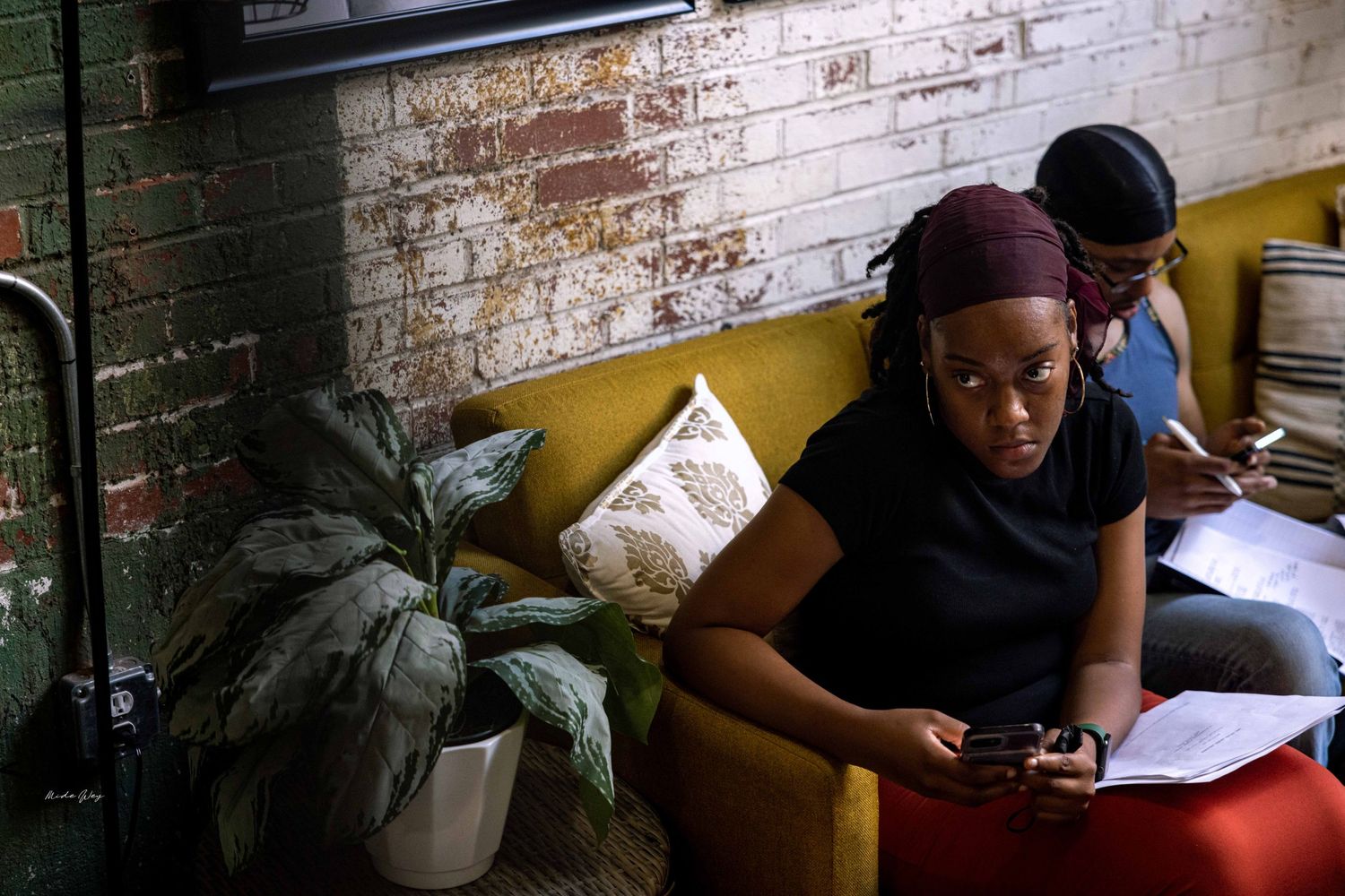 People working in a cozy corner with exposed brick walls and indoor plants.