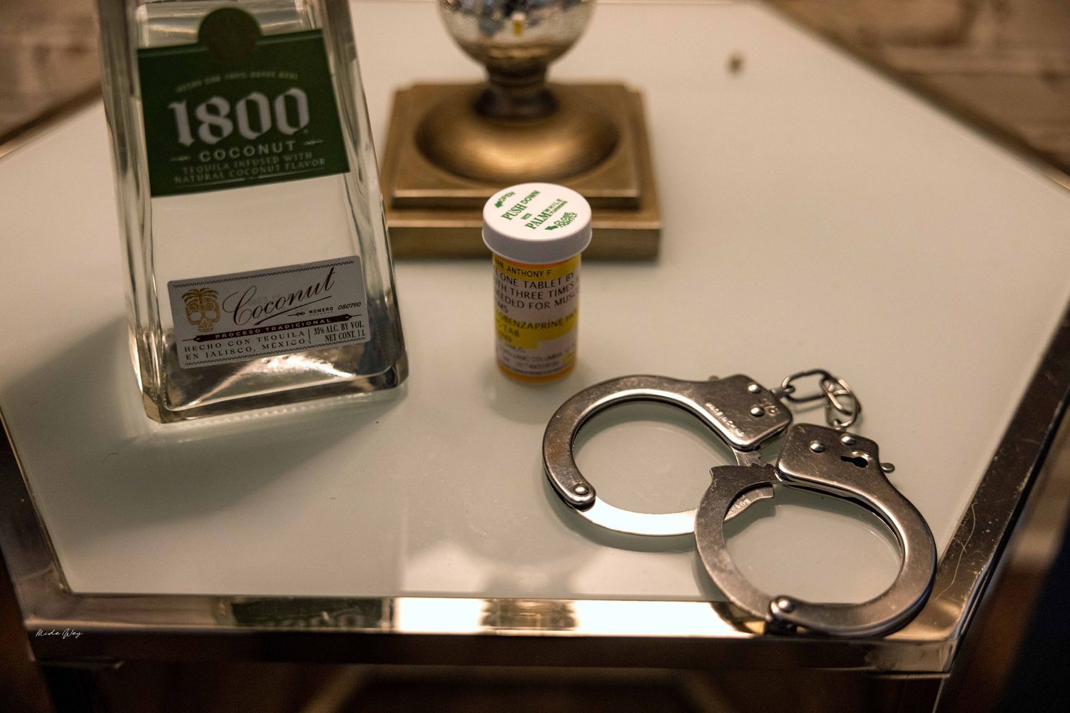 Close-up of glass bottles and handcuffs arranged on a reflective surface.