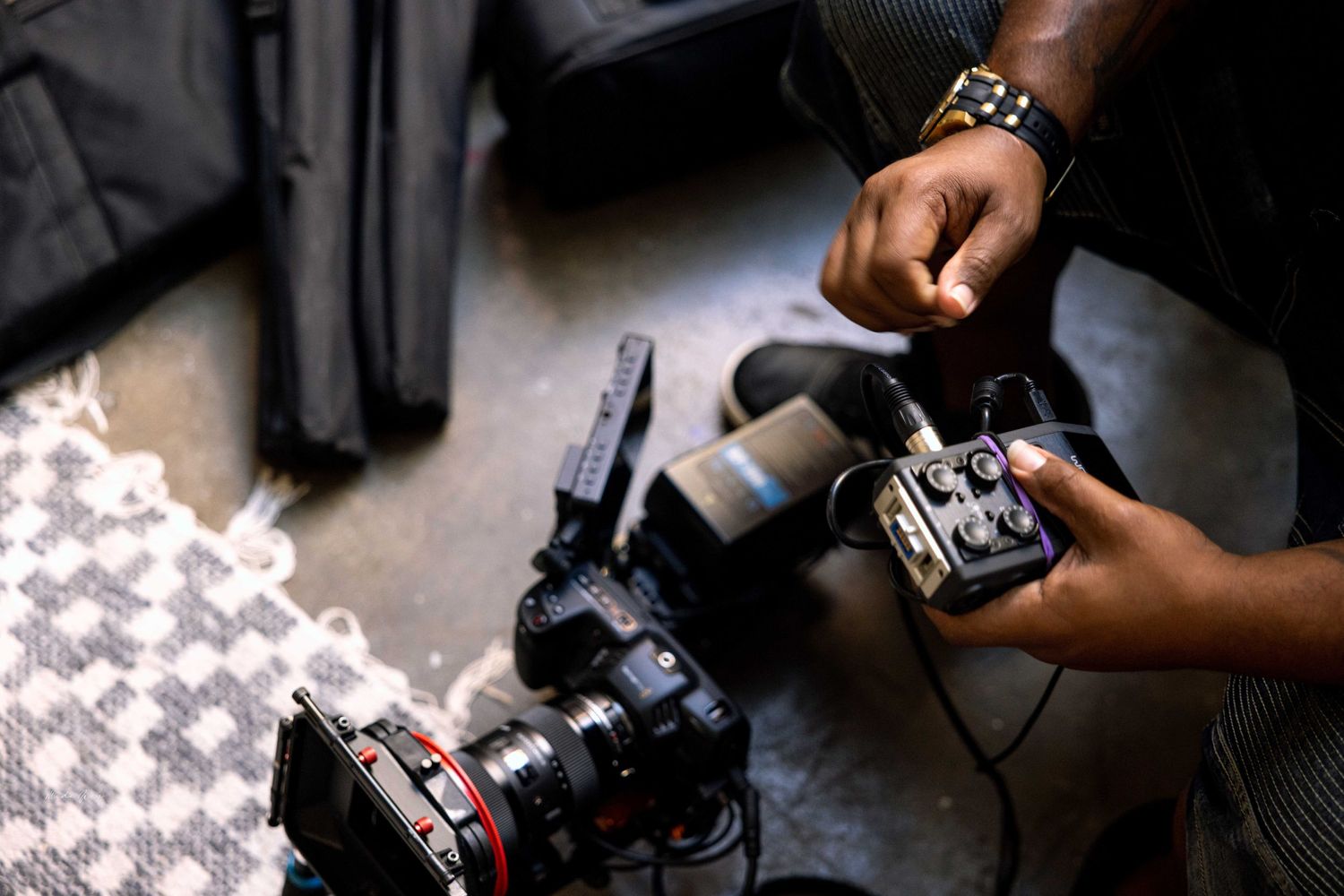 Camera equipment and lighting setup with hands adjusting settings in a dim environment.
