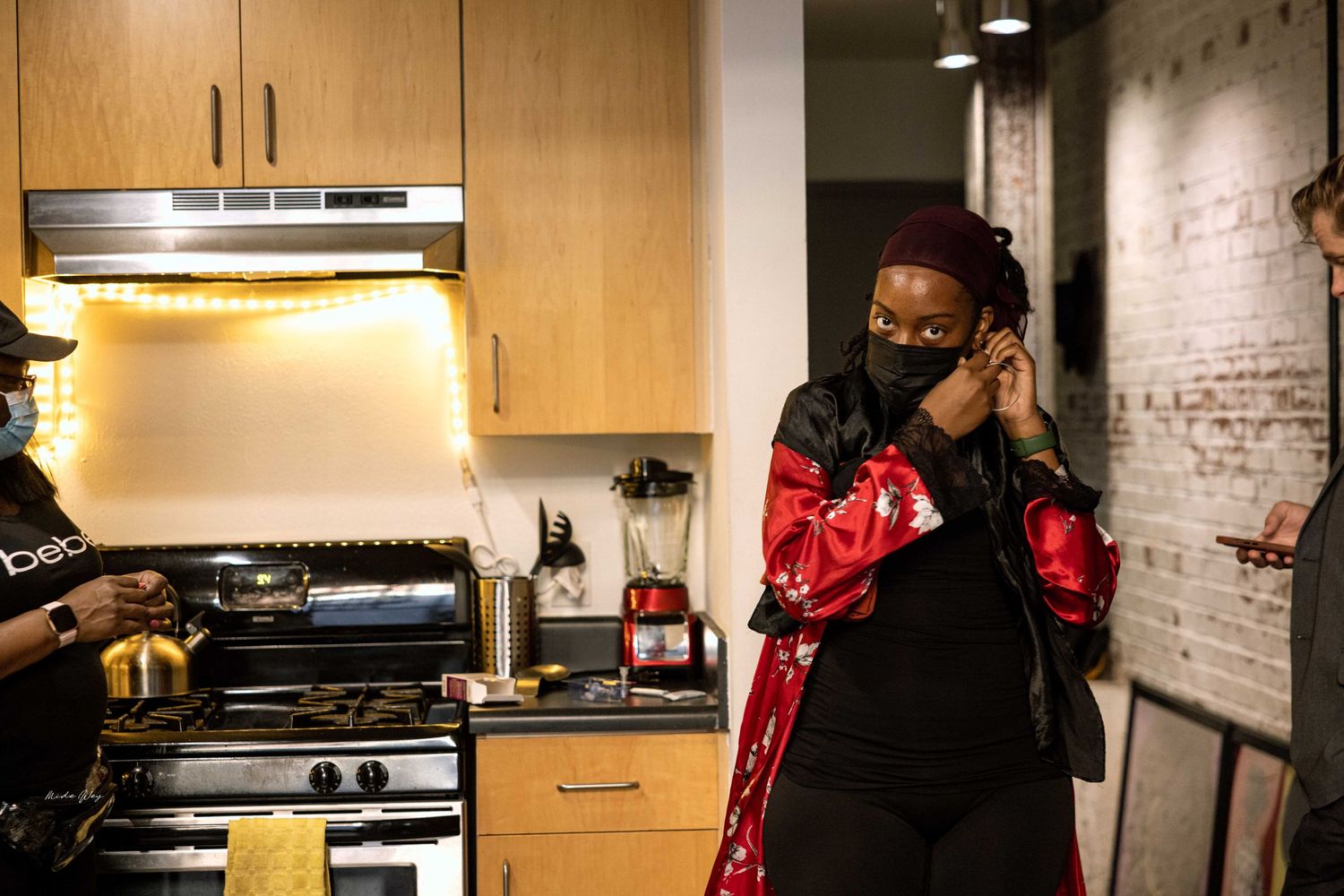 Person in kitchen with wooden cabinets and stainless steel appliances wearing mask.